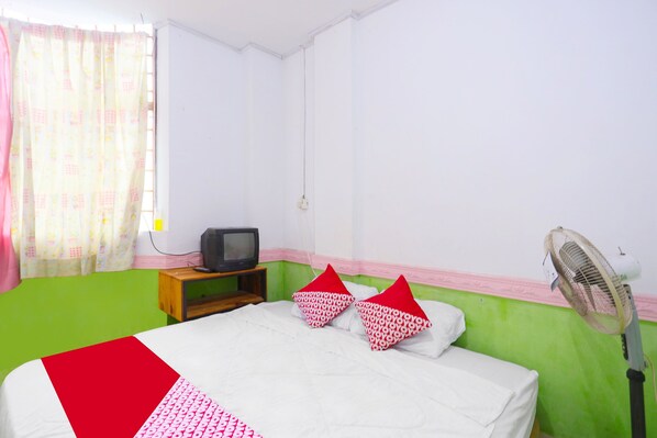 Une chambre avec un lit, une télévision, un ventilateur et une fenêtre avec des rideaux.