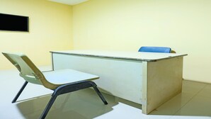 Una habitación con escritorio, una silla, televisor montado en la pared y piso de baldosas.
