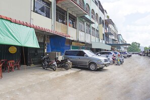Une rue bordée de voitures et de motos garées, des immeubles avec des enseignes commerciales, et une bâche verte recouvrant une structure.