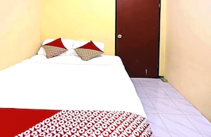 Un petit lit bien fait, avec des oreillers à motifs et une couvre-lit rouge et blanche, dans une pièce aux murs jaunes et à la porte marron.