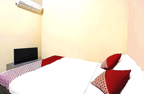 A hotel room with a bed, a flat-screen TV, and an air conditioner on the wall.