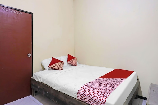 Un lit simple avec une literie blanche et des touches de rouge, une tête de lit en bois et une porte rouge.