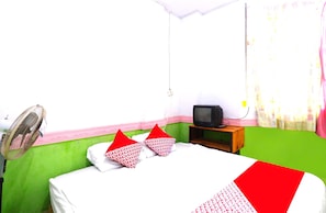 Une chambre avec un lit, une télévision, un ventilateur et une fenêtre avec des rideaux.