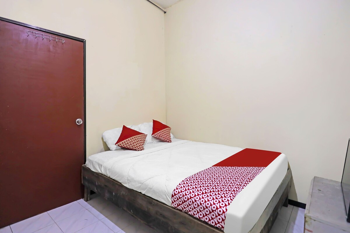 A small, single-bed room with a wooden headboard, white bedding, and a red and white patterned throw blanket.