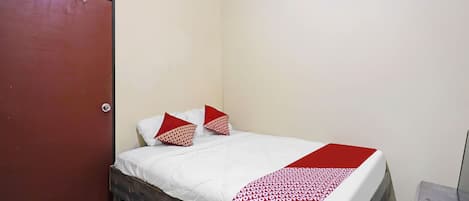 Una habitación pequeña con cama individual, cabecera de madera, ropa de cama blanca y una manta de patchwork roja y blanca.