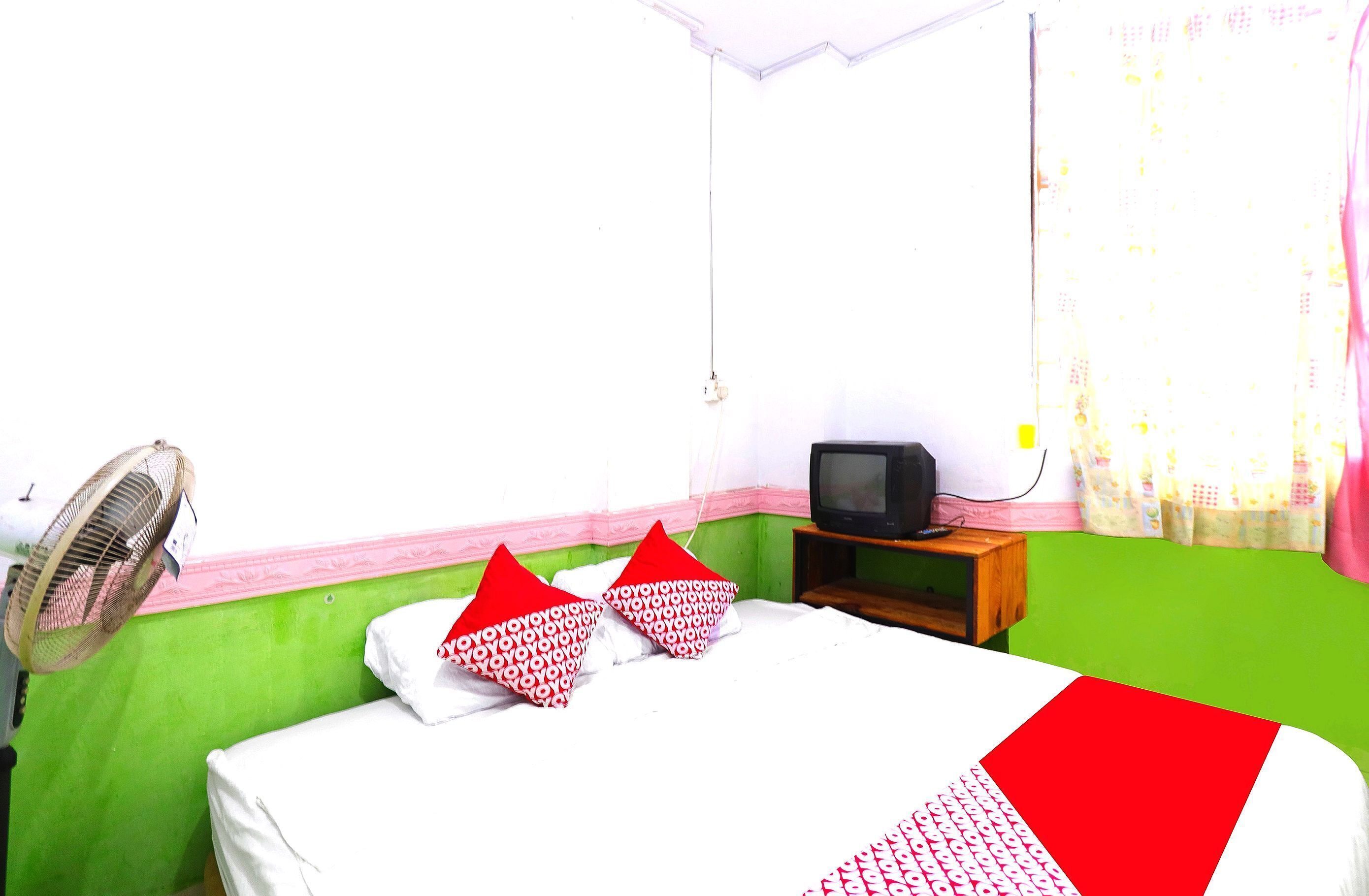 A room with a bed, a television, a fan, and a window with curtains.