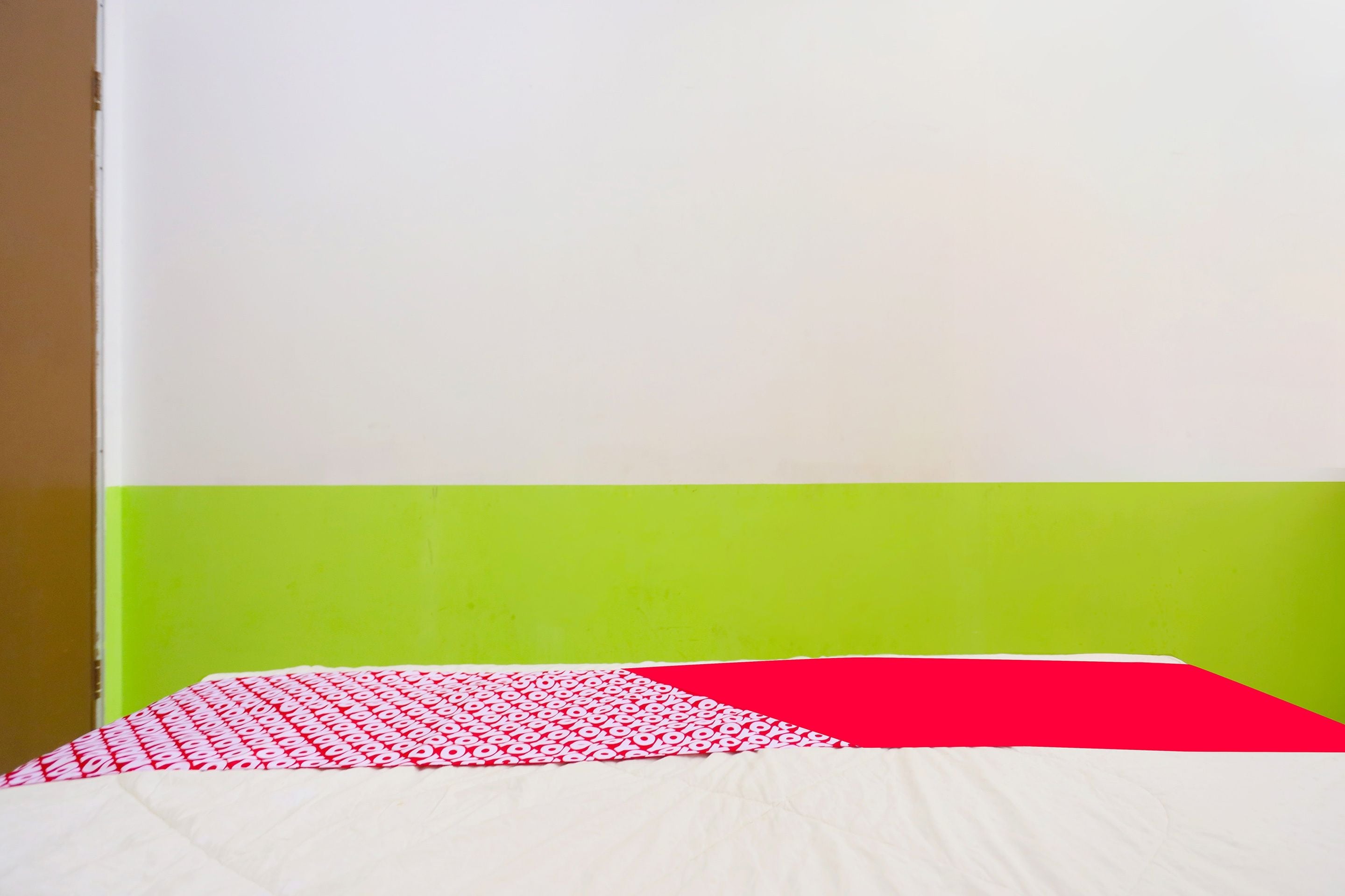 A bed with a white and red patterned bedspread, a green wall, and a white ceiling.