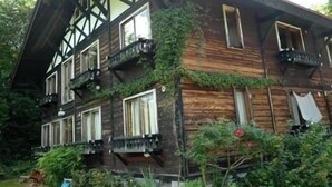 A wooden house with multiple balconies and windows, surrounded by greenery. - Pension Swiss (Kaminoyama)
