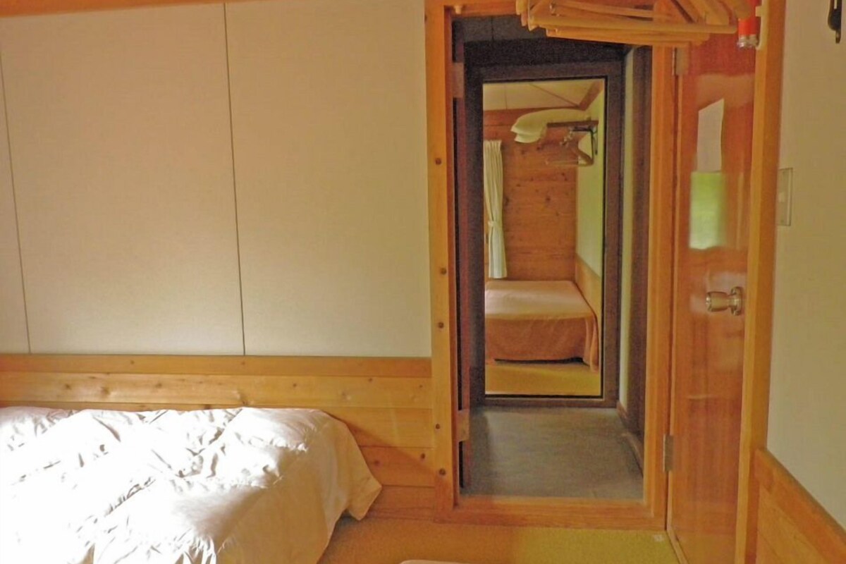 A bedroom with a wooden bed, a small bedside table, a mirror, and a door leading to a bathroom.