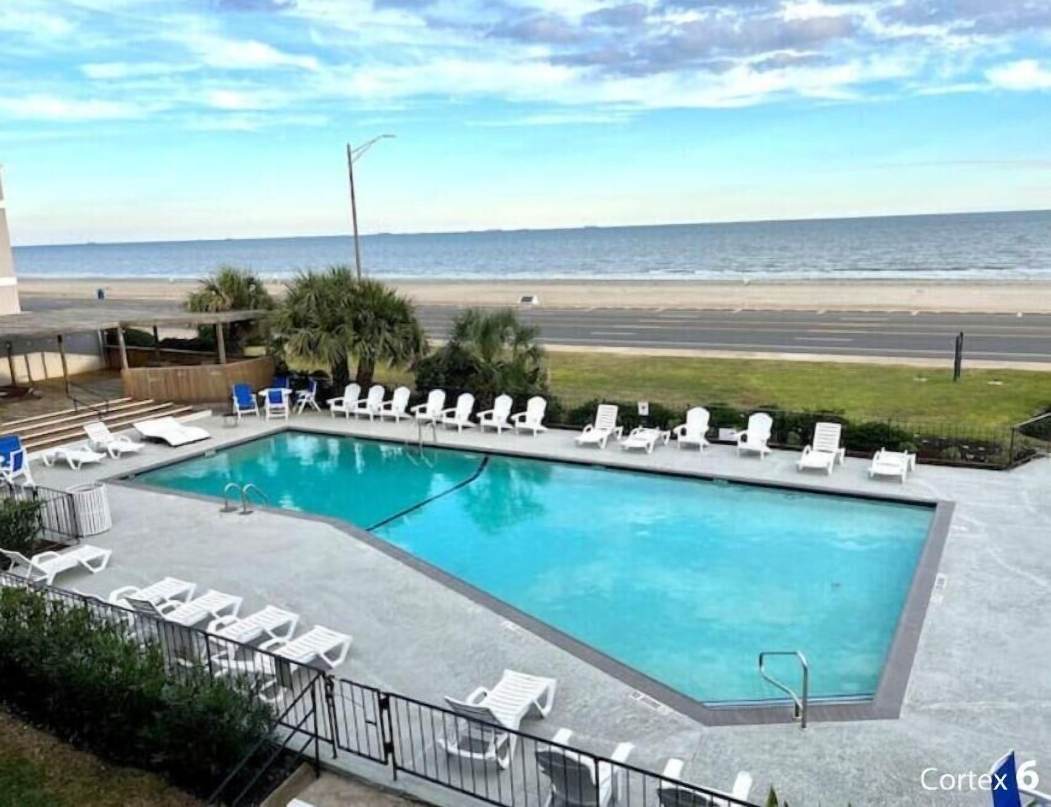 Una piscina con sillones de descanso y vista a la playa y al océano.