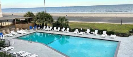 Una piscina con sillones de descanso y vista a la playa y al océano.