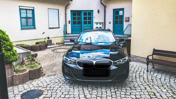 A black car parked in front of a building with blue doors and windows.