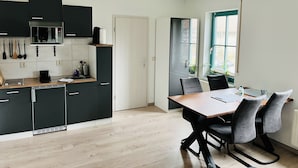 A modern kitchen with dark cabinets, a microwave, and a coffee maker. There is a dining table with chairs and a window with a view of the outside.