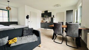 A modern, compact living space with a bed, a sofa, a dining area, and a kitchenette.
