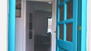 A teal door with an Airbnb logo, a black mat at the entrance, and a view into a room with a dining table and chairs.