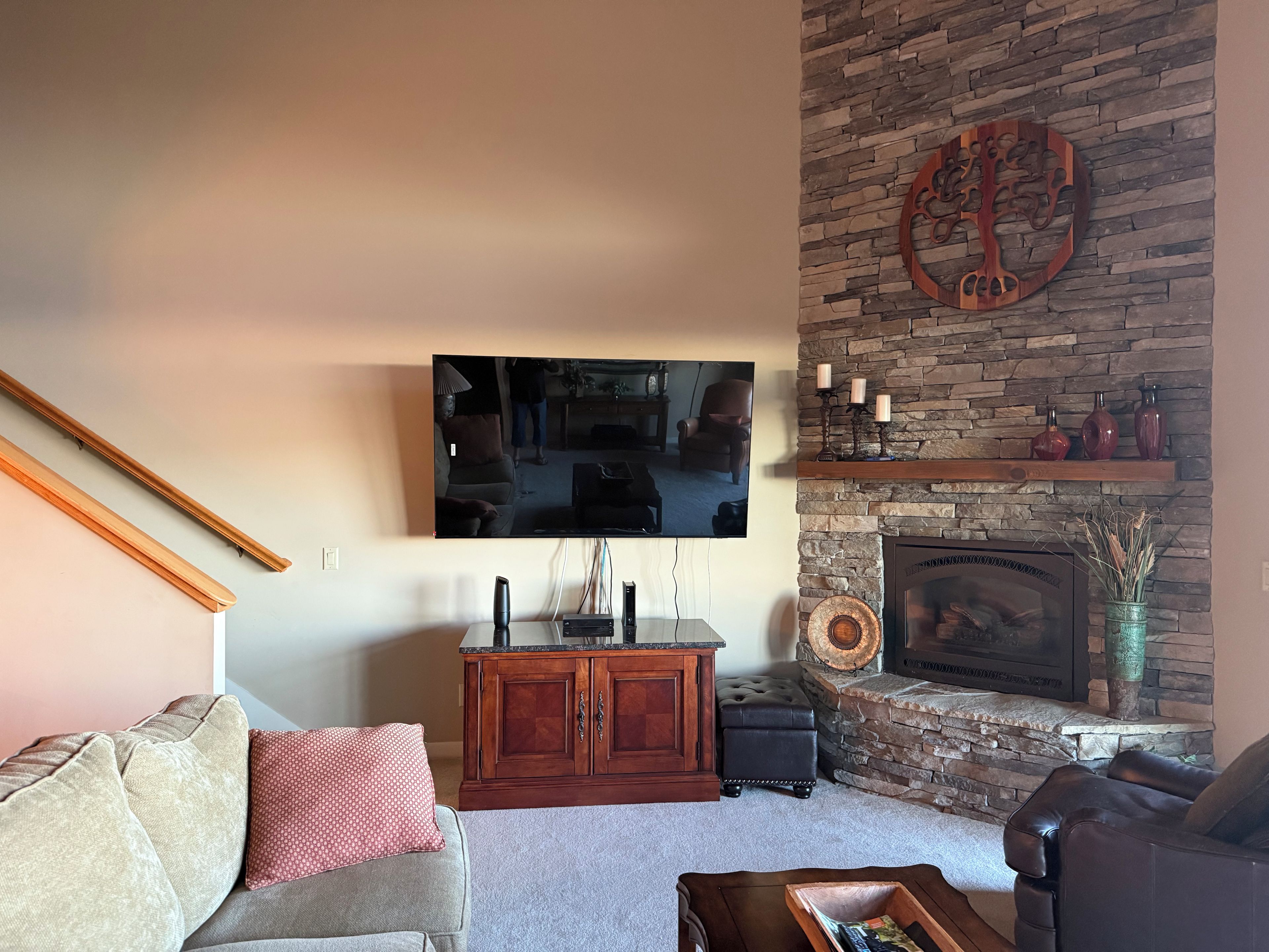 A living room with a stone fireplace, a flat-screen TV mounted on the wall, and a wooden cabinet.