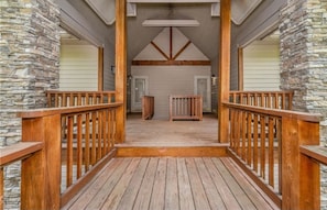 A wooden deck with stone walls, leading to a door with a small table and a bench.