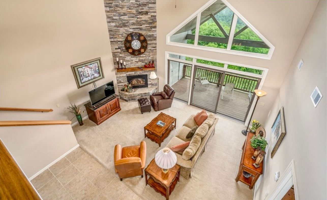 A spacious living room with a stone fireplace, a large window, and a balcony.