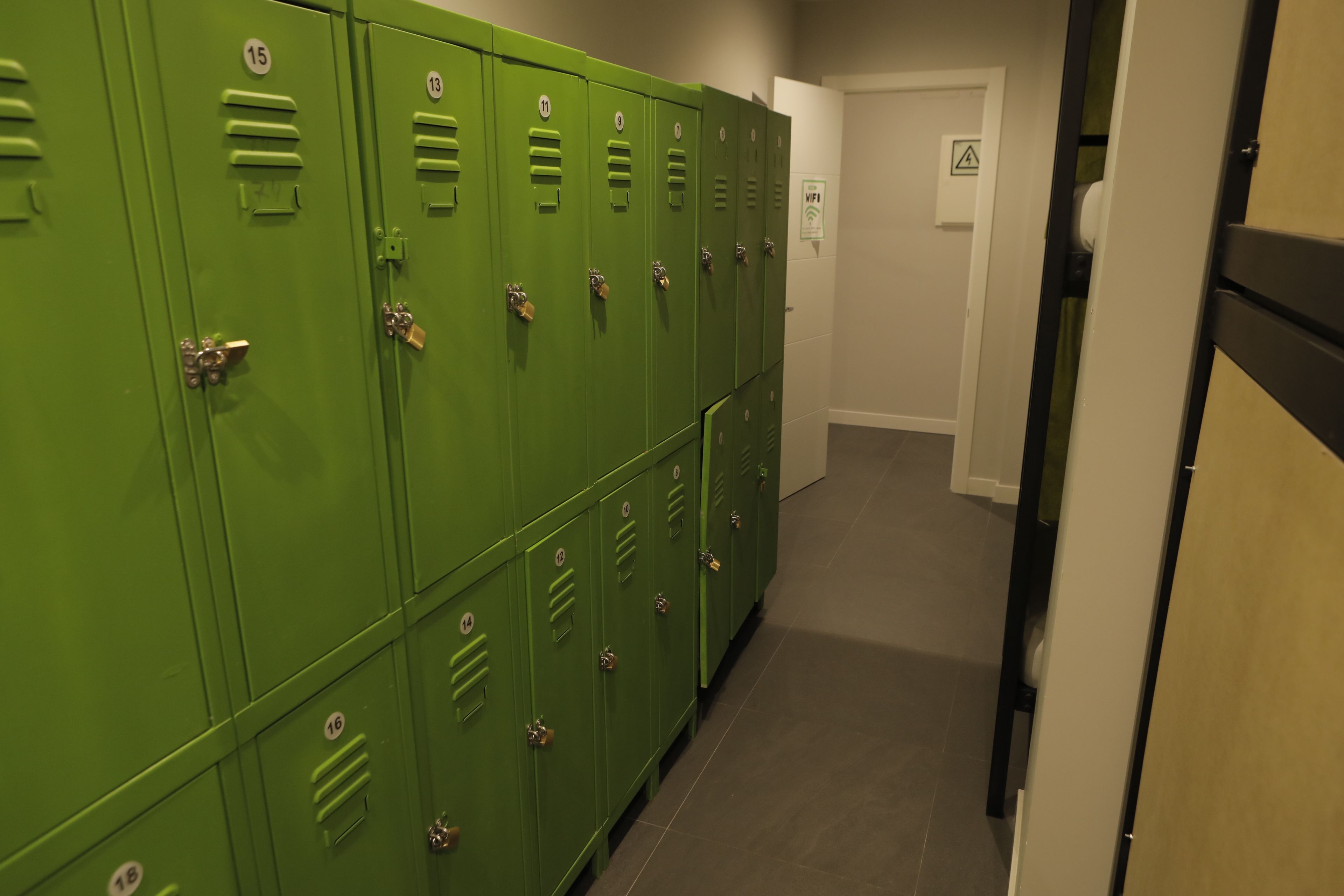 A hallway with green lockers numbered 9 to 18, a door with a WiFi sign, and a tiled floor.