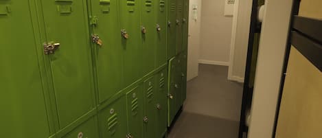 A hallway with green lockers numbered 9 to 18, a door with a WiFi sign, and a tiled floor.
