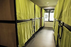 A corridor with bunk beds, each with a yellow curtain, leading to a window. - MYD Madriz Hostel (Madrid)