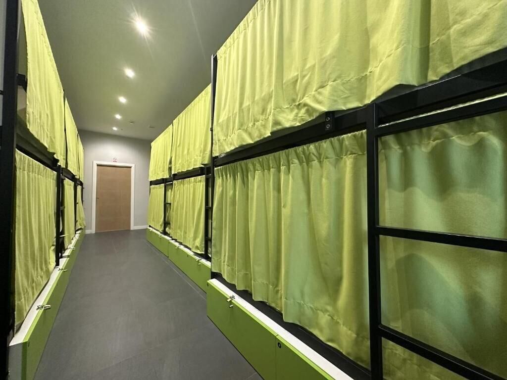 A corridor with bunk beds, each with a green curtain, and a door at the end.