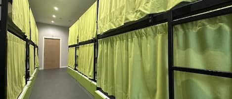 A corridor with bunk beds, each with a green curtain, and a door at the end.