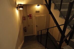 Una escalera con barandilla, una puerta y una lámpara fijada a la pared.