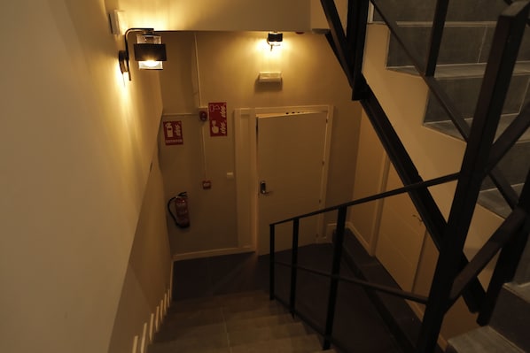 A staircase with a handrail leading to a landing where a door and a fire extinguisher are mounted on the wall. - MYD Madriz Hostel (Madrid)