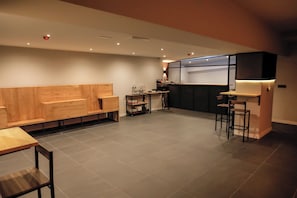 A modern kitchen with a wooden bench seating area, a bar counter, and a small kitchenette. - MYD Madriz Hostel (Madrid)