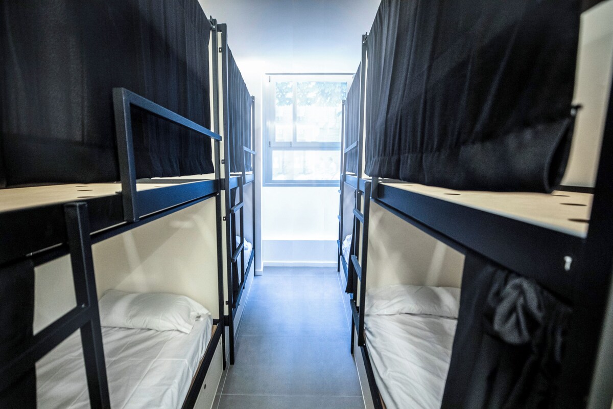 Ein Korridor mit Etagenbetten, einem Fenster am Ende und einem gefliesten Boden.