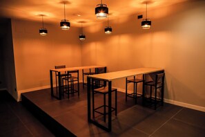 Un espace repas comprenant une longue table et quatre chaises, un éclairage suspendu et un plancher foncé.