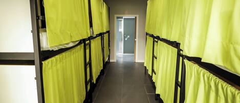 A corridor with bunk beds, each with a yellow curtain, leading to a door at the end.