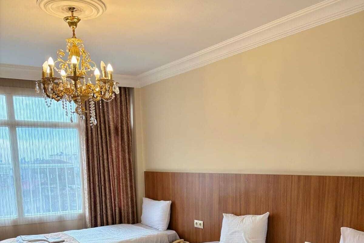 A hotel room with three beds, a chandelier, and a large window with curtains.