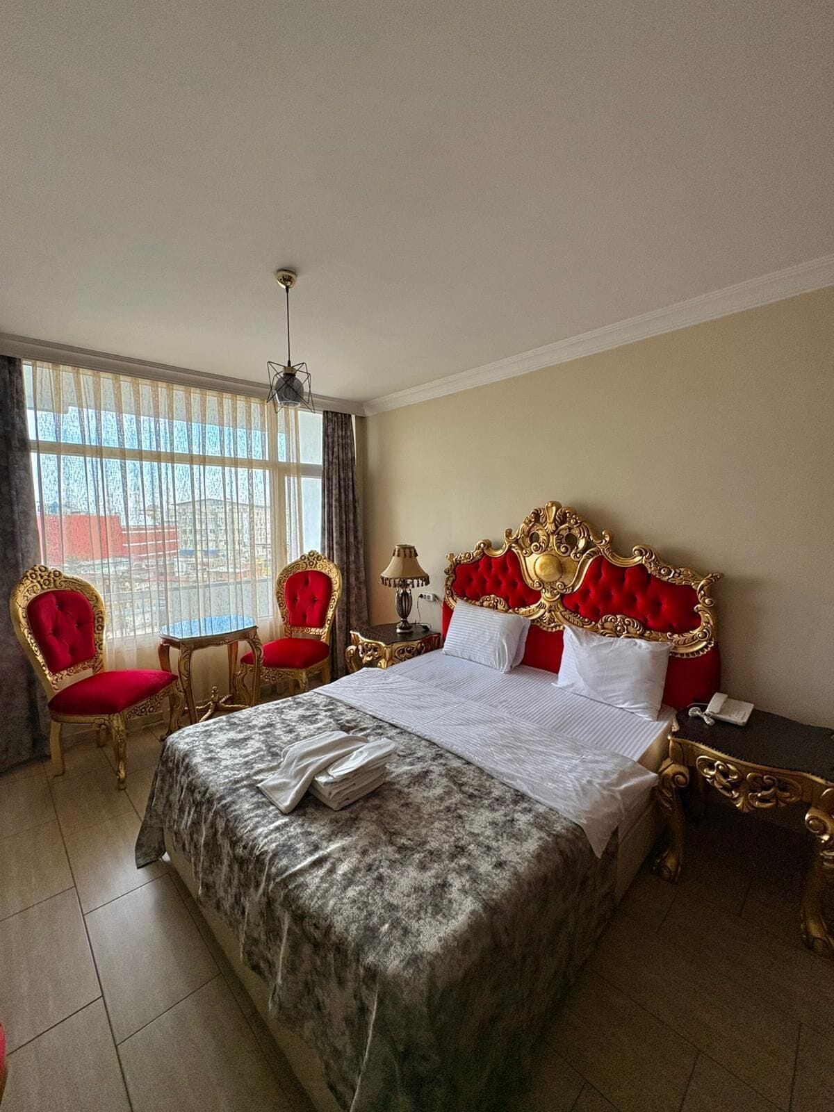 Habitación de hotel con una cama grande, dos sillones tapizados en rojo, una mesita y una mesilla de noche.