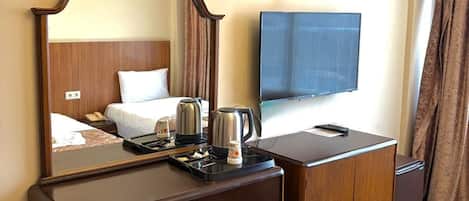 Habitación de hotel con escritorio de madera, espejo, televisor de pantalla plana, minibar y cama con cabecero.