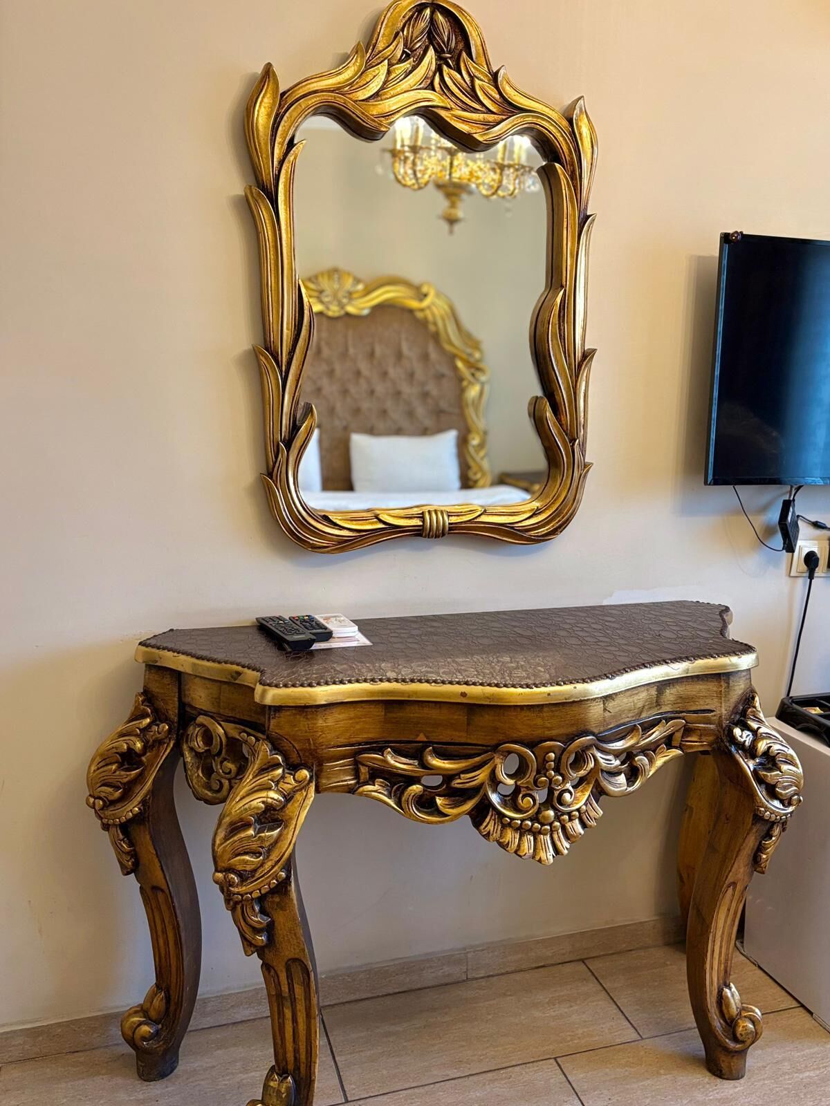 A room with a large ornate mirror, a television, and a small table with a remote control on it.