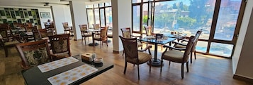 Un comedor amplio con mesas y sillas de madera, ventanas grandes que ofrecen vistas a la ciudad, y una decoración interior moderna y elegante.