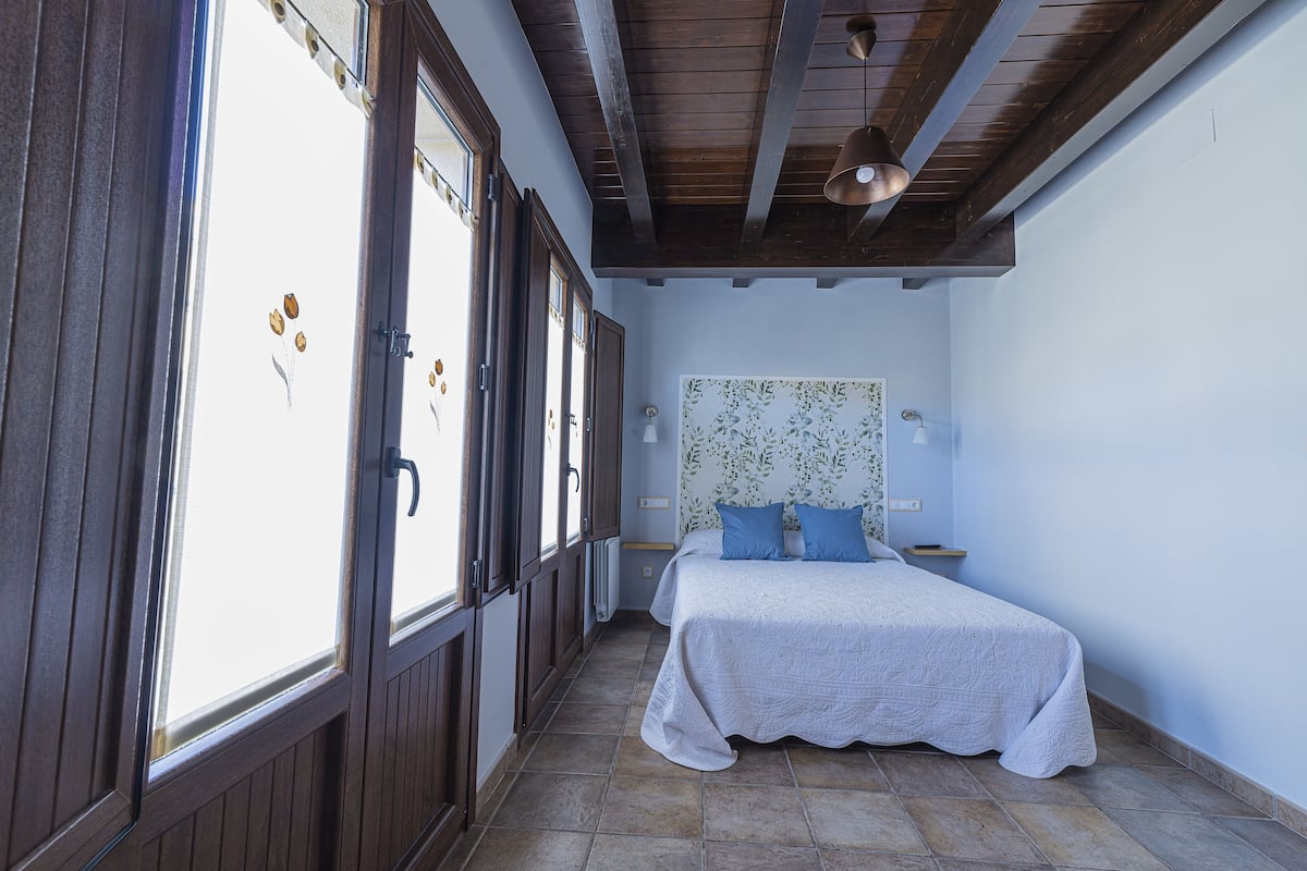 Ein Schlafzimmer mit einem Bett, einem Fenster und einer Holzbalkendecke.