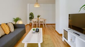 A modern living room with a sofa, coffee table, TV, and dining area.
