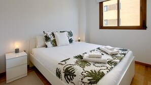 A bedroom with a bed, a nightstand, a window, and a view of a building outside.