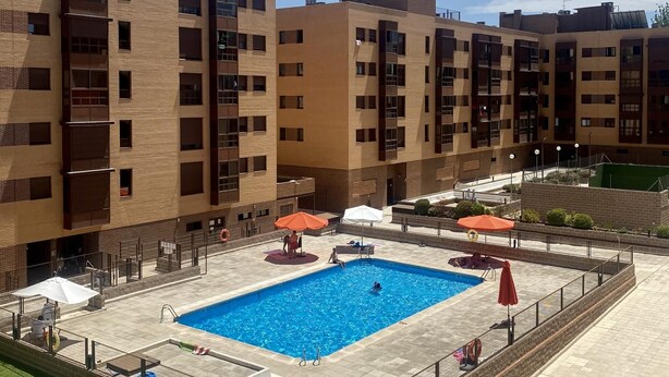 A modern building with a swimming pool, outdoor seating, and a fenced area.