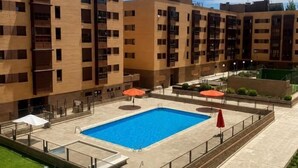 A modern building with a rectangular pool, outdoor seating, and a fenced patio area.