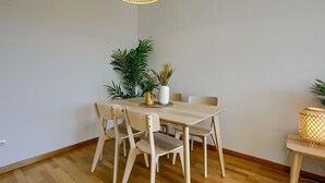 A dining area with a wooden table and chairs, a hanging light fixture, and potted plants.