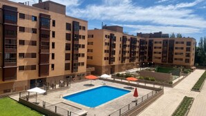 A modern apartment building with a swimming pool, outdoor seating, and a well-maintained lawn.