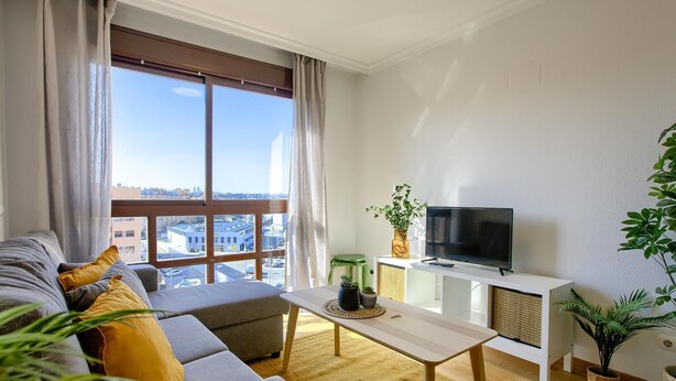A modern living room with a sofa, a coffee table, a TV, and a view of the city through large windows.