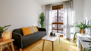 A modern living room with a grey sofa, a small white table, and a large window with curtains. - Charming Madrid Airport III (Madrid)