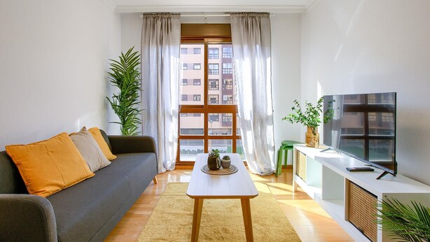 A modern living room with a grey sofa, a small white table, and a TV on a white cabinet. - Charming Madrid Airport III (Madrid)
