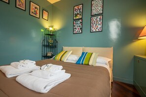 A hotel room with a bed, towels, pillows, a nightstand, a lamp, and wall art. - Tiffany's Apartment Flaminio (Roma)