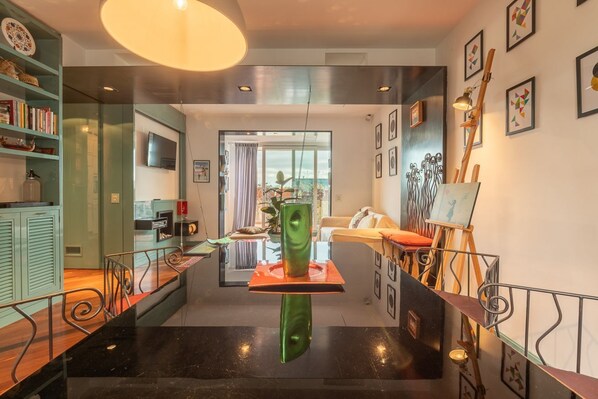 A modern interior with a central reflective sculpture, a staircase with metal railings, and a view of the outdoors through a glass door.